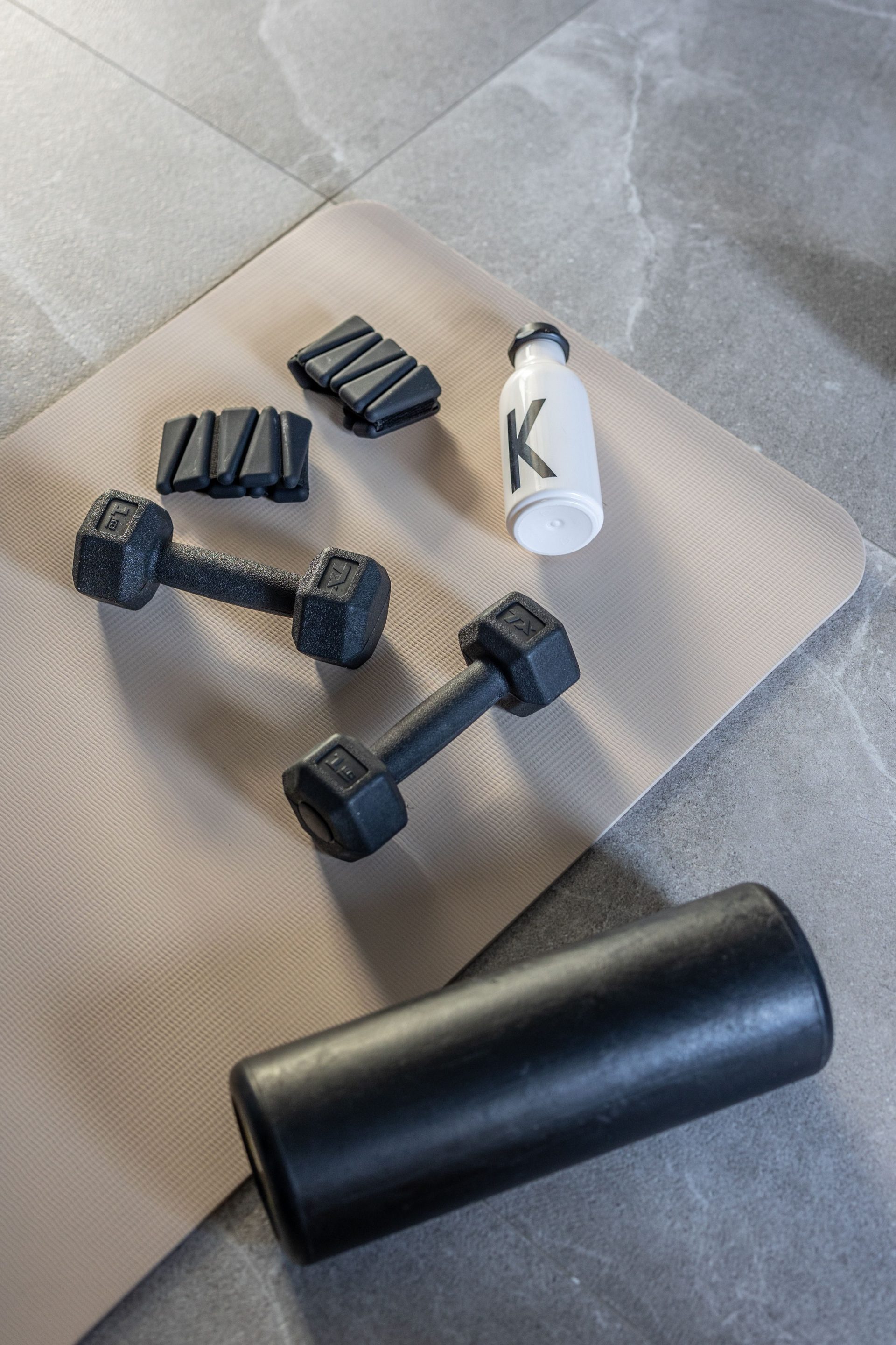 Flat lay of dumbbells, weights, and bottle on mat for fitness home workout.