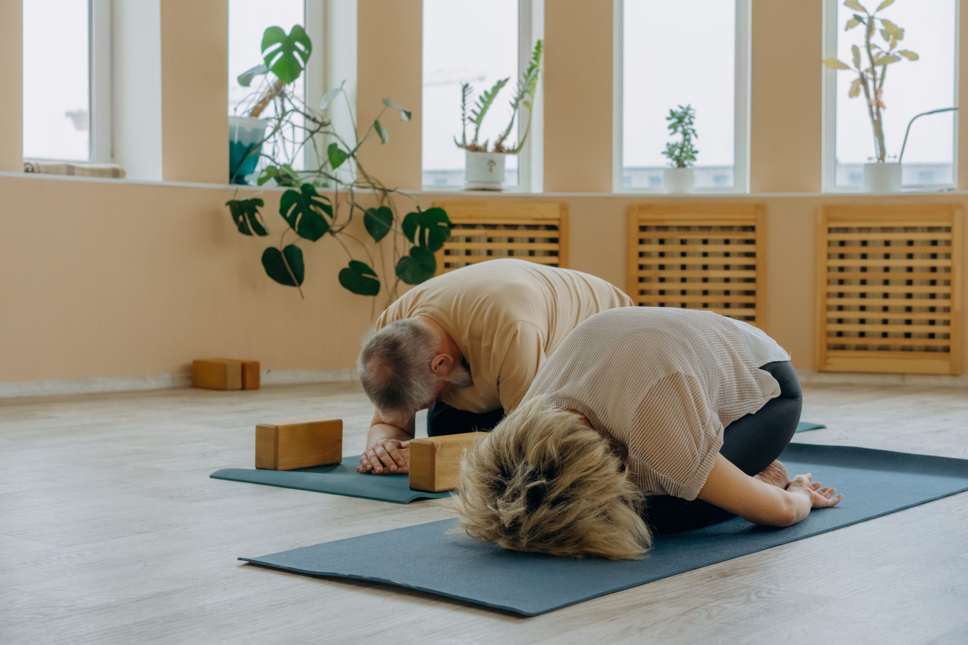 Senior couple practicing yoga together indoors, focusing on stretching and wellness.