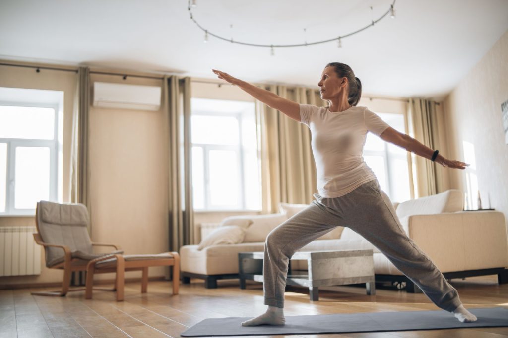 Elderly woman enjoying yoga and stretching exercises at home, promoting wellness and healthy living.